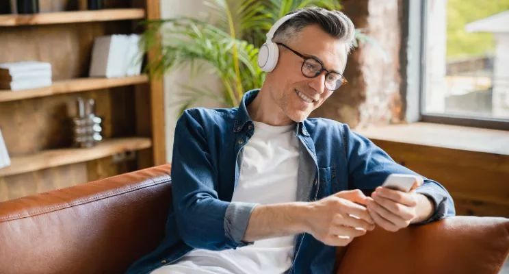 Man with glasses wearing headphones looking at phone on couch