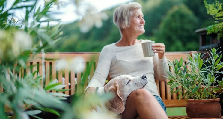 Woman drinking coffee look off in distance with sleeping dog in her lap